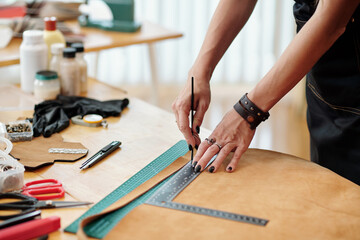 Hands of creative young woman cutting leather piece in stripes for making bag