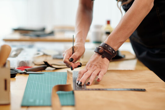 Hands of skilled young woman cutting leather in stripes when making bag for customer