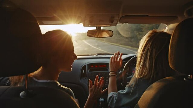 Two happy female friends sing song enjoying traveling in car. Sitting in front seat having fun road trip. Girls driving car dancing. youth, friendship, dancing music while driving her car at sunset.