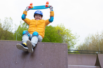 portrait of a smiling schoolboy in a safety helmet with a bright blue skateboard, an urban cruiser...