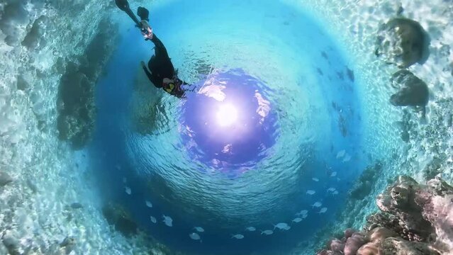 10 Woman snorkeling in full body suit as sun protection in tropical sea over corals in coral garden with a rabbit hole effect in 360 degree video camera mode