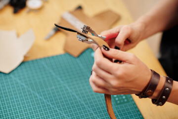 Hands of craftsperson perforating leather belt with special tool