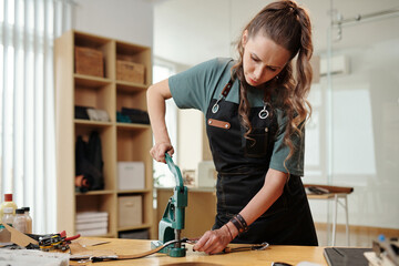 Leather worker using hand press when making holes in leather bag handle