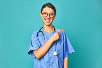 A young nurse woman isolated smiling and pointing aside, showing something at blank space.