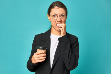 A young caucasian business woman holds a takeaway coffee biting fingernails, nervous and very...