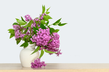 In a white gypsum vase is a bouquet of lilacs. On a wooden table.