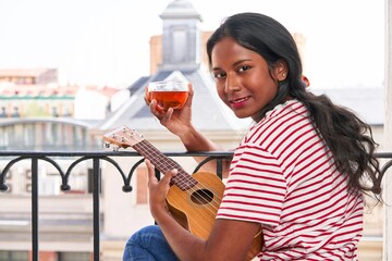 Indian woman playing ukulele on windowsill drinking a tea cup