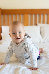Fototapeta premium An 8 month old happy and smiling baby sitting independently on a bed