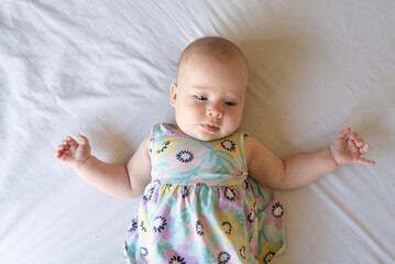 A top down image of a content and aware baby girl of 4 months old lying on a bed