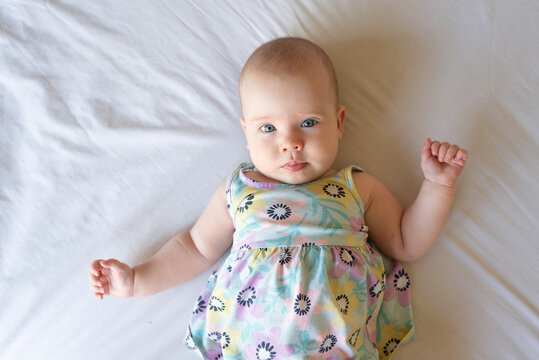A top down image of a content and aware baby girl of 4 months old lying on a bed