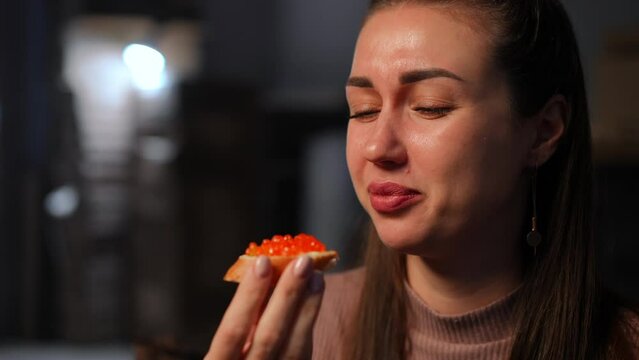 Close-up Caucasian young woman eating sandwich with spoiled salmon caviar making dissatisfied facial expression. Unsatisfied beautiful lady with bad taste toast indoors