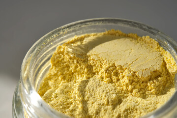 An open jar of a yellow turmeric facial scrub showing off its texture.