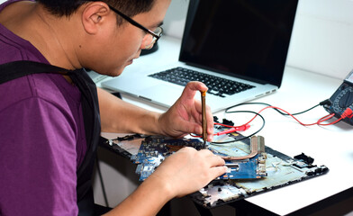 Computer technician wearing eyeglasses Laptop motherboard repairman is using a screwdriver to dismantle a motherboard for repairs on his desk. Repairing the board. Electronic technician.

