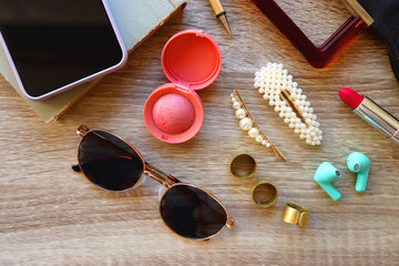 Fototapeta na wymiar Handbag, sunglasses, beauty products, pearl hair clips, rings, pen, earbuds, book and phone on wooden background. Top view.