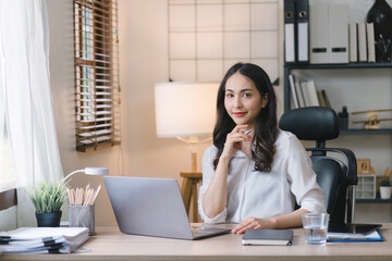 Portrait of a young, cheerful, happy, positive, cute, and beautiful Asian millennial businesswoman Working on Financial and Marketing Projects while sitting indoors in a home office.