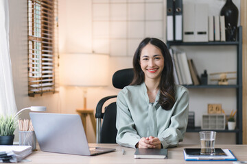 Obraz na płótnie Canvas Portrait of a young, cheerful, happy, positive, cute, and beautiful Asian millennial businesswoman Working on Financial and Marketing Projects while sitting indoors in a home office.