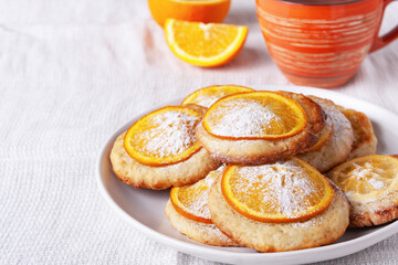 homemade orange cookies, orange cup with tea on white tablecloth, copy space