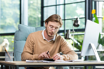 Accounting, audit. A young man works with documents and bills in the office. Calculates and checks...