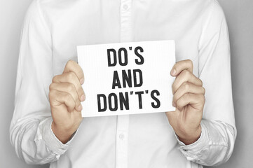 Man holding a paper card with text DO S AND DONTS