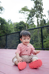 A Malay baby boy is posing with his new clothes and sit on red wooden floor