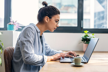 Beautiful attractive entrepreneur woman working with laptop while drinking coffee in the living room at home.