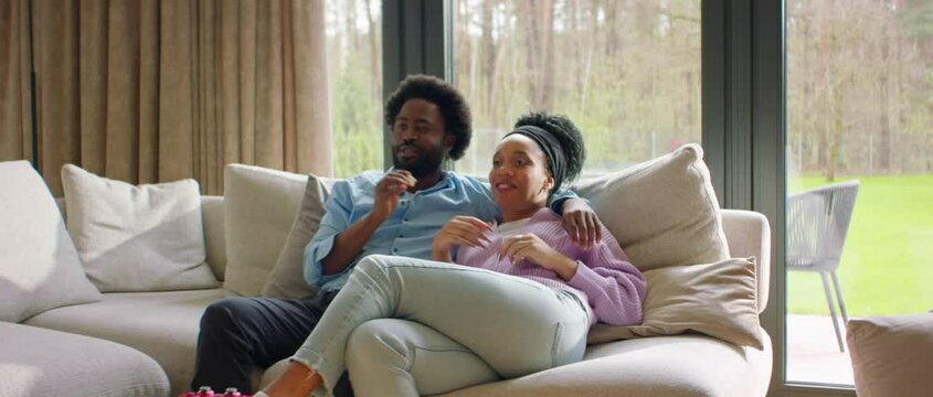 Portrait of African-American black couple or family watching TV at home, enjoying popcorn, discussing the movie Generative AI