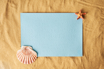 Blank paper card on sandy beach with seashells and starfish. Summer time concept, vacation