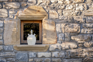 a white botijo on the exterior window sill of a stone village house, typical spanish clay jug to keep the water cool in summer, rustic atmosphere