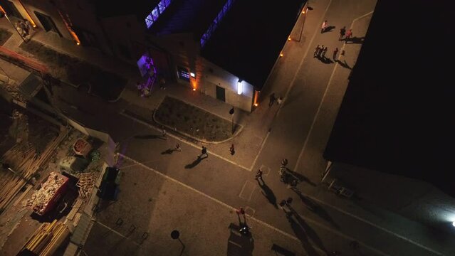 Pedestrian zone aerial drone shot Top down Night, lights, people walking. Aerial drone shot at night evening people walking strolling between houses.