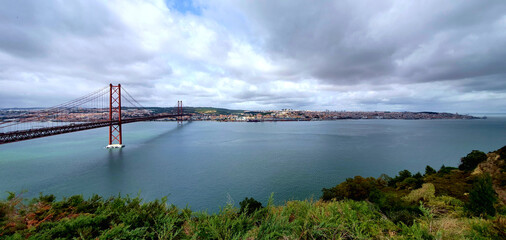 Panorama view of the 25 April bridge during a cloudy afternoon in Lisbon, Portugal