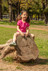 Cheerful little girl sitting on a tree in the park