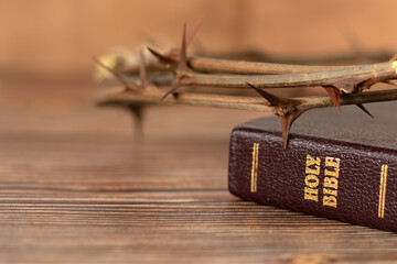 Thorn crown on top of a closed holy bible book with golden text on wooden table. A closeup. Selective focus. Christian biblical concept of Jesus Christ's crucifixion, suffering, and salvation.