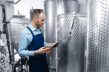 Worker man examining quality of craft beer at brewery. Inspector checking drink in alcohol brewery manufacturing factory - Powered by Adobe