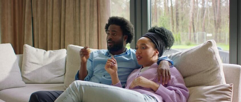 Portrait of African-American black couple or family watching TV at home, enjoying popcorn, discussing the movie Generative AI