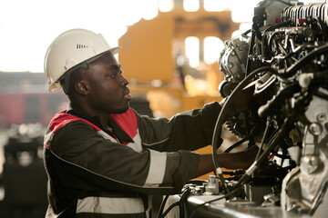 Fototapeta na wymiar Side view of young male engineer in workwear checking hydraulic hoses and other details of indistrial machine while working in factory
