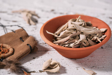 Loose White Sage leaves (Salvia apiana) in a clay bowl and medicinal pouch on old white wood