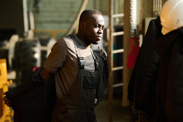 Young African American worker of industrial factory putting on workwear in changing room before...