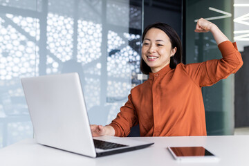 Naklejka na ściany i meble Successful asian businesswoman working inside office with laptop, female employee received online message victory and good achievement results, female partner holding hands up celebrating triumph.