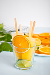 Fruit orange citrus popsicles ice pops in glass and slices of orange on plate on the background.