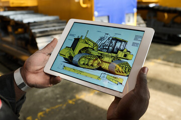 Close-up of tablet with picture of bulldozer on screen held by young African American engineer or...