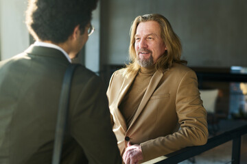 Focus on smiling mature businessman talking to young multi-ethnic male colleague during negotiation...