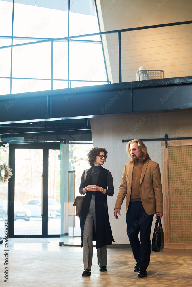 Aufkleber Two mature colleagues in quiet luxury attire discussing working points while walking along spacious corridor or lounge in business center