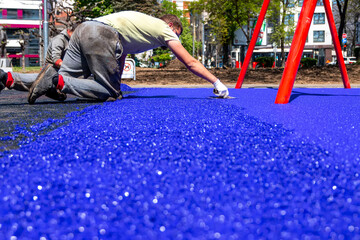Belgrade, Serbia - April 28, 2023: New childrens playground under construction. A mason hand with trowel  spreading and leveling soft rubber crumbs rubber mulch .for children's playground. - obrazy, fototapety, plakaty
