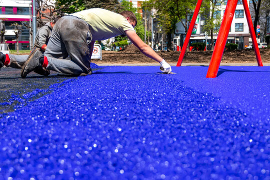 Belgrade, Serbia - April 28, 2023: New childrens playground under construction. A mason hand with trowel spreading and leveling soft rubber crumbs rubber mulch .for children's playground. - Powered by Adobe