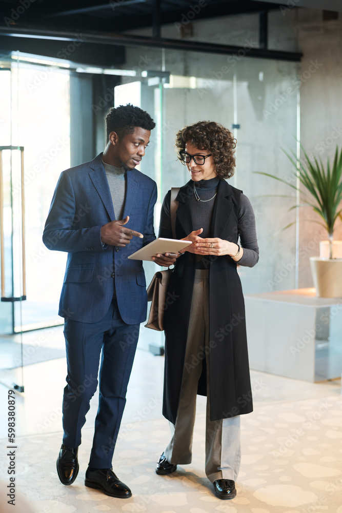 Poster Young confident broker in suit explaining female colleague in quiet luxury apparel online data during presentation while pointing at tablet screen