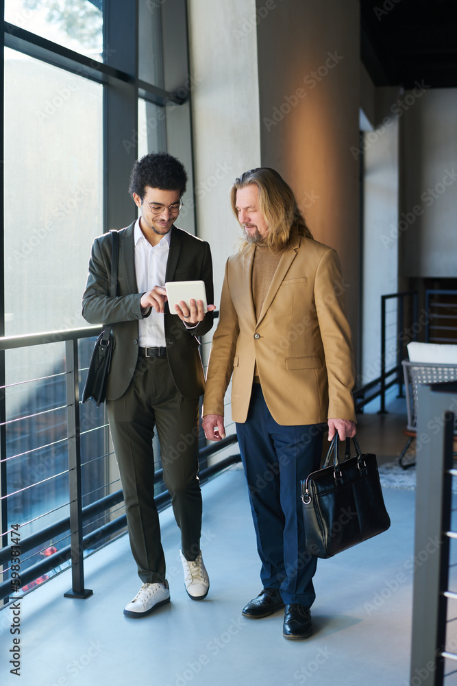 Aufkleber two intercultural businessmen in formalwear discussing online financial data in tablet while walking