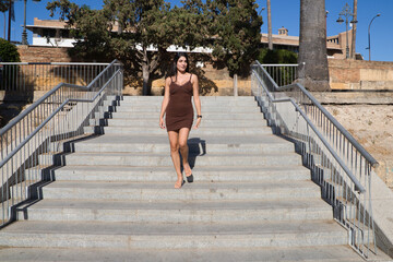 young and beautiful woman from south america dressed in a short dress is walking down a staircase. The woman is happy because she is on vacation in Europe. Travel and vacation.