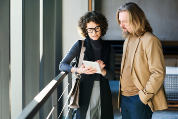 Two mature managers in smart casualwear looking through financial data on screen of tablet held by...