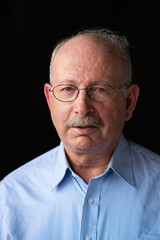 Obraz premium Grey haired senior man with mustache wearing eyeglasses against black background