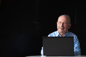 Grey haired senior man using laptop computer while smiling and thinking